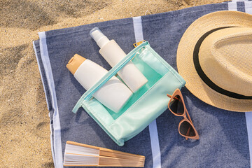 Bottles of sunscreen cream with hat and sunglasses on sandy background