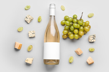 Bottle of tasty wine with blank label and grape on grey background