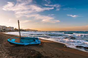 traditional Greek fishing boat on the shore at sunset on Crete, Greece.