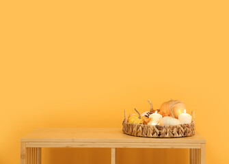 Burning candles and pumpkins on table near orange wall