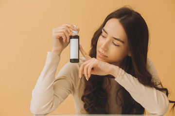 Photo mockup. Pretty brunette woman holding bottle of cosmetics isolated on beige background.