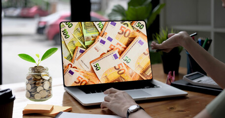 Mujer exitosa observando en su laptop los miles de euros que ha ganado con su venta online. Las monedas de su frasco se multiplican como una planta que no para de crecer. Su mano recibe la ganancia.