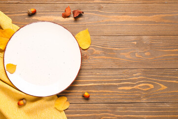 Empty plate with autumn leaves and acorns on wooden background