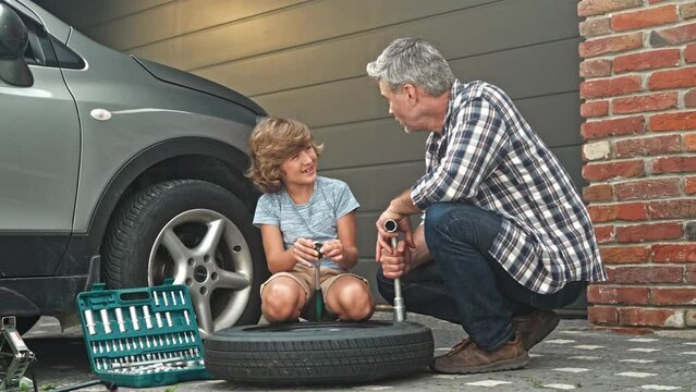 Handsome Caucasian dad talking with his loving son near their broken car outside. People holding mechanical tools to repair auto during conversation. Young kid helping his father work outside.
