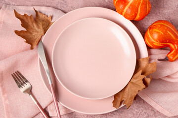 Autumn table setting with pumpkins and dry leaves on pink grunge background