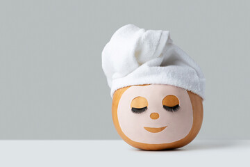 Pumpkin with cosmetic mask and eyelashes in a towel