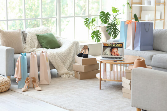 Interior of stylish living room with shopping bags, boxes, new clothes and laptop on table