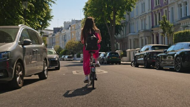 Young tourist woman enjoys riding bicycle on the street of London Portobello road in summer day. Urban cycle chic and ecological transportation by bike