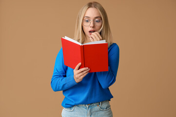 Beautiful young shocked woman with book on brown background