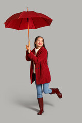 Beautiful young Asian woman with umbrella on grey background