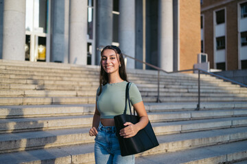 Portrait of young student woman outdoor at university. She is standing with a handbag looking at the camera. 