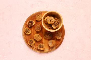 Wooden board and bowl with sweet dried figs on pink background