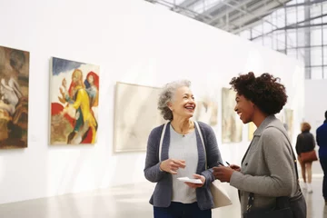 Foto op Plexiglas Females, adult woman and elegant lady visitors art gallery discussion artwork in exhibition at a modern museum of contemporary art. Abstract painting in the background on a white wall © Garnar