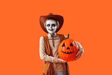 Little boy dressed for Halloween as cowboy with pumpkin on orange background