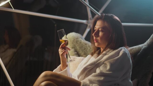 Depressed woman drinks alcoholic drink sitting in armchair