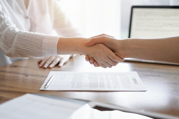 Business people shaking hands above contract papers just signed on the wooden table, close up....