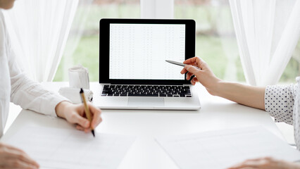 Two accountants using a laptop computer for counting taxes at white desk in office. Business Woman pointing into screen with a pen. Teamwork in business audit and finance