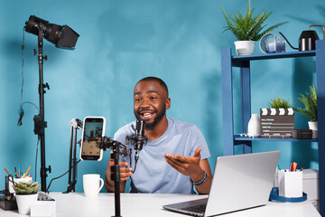 Blogger filming video with smartphone and speaking to internet channel subscribers. African...