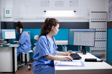 Caucasian nurse sitting at clinic desk, writing data in appointment table list. Focused medical...