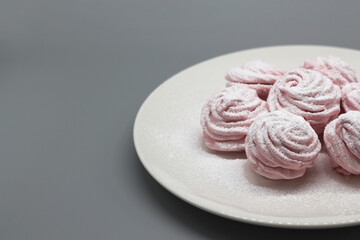 Delicate handmade pink marshmallows on a white plate on a gray background.