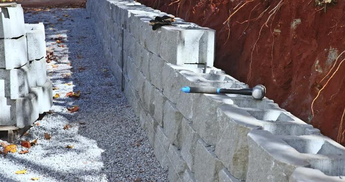 Construction worker lifted concrete block positioned it on retaining wall.