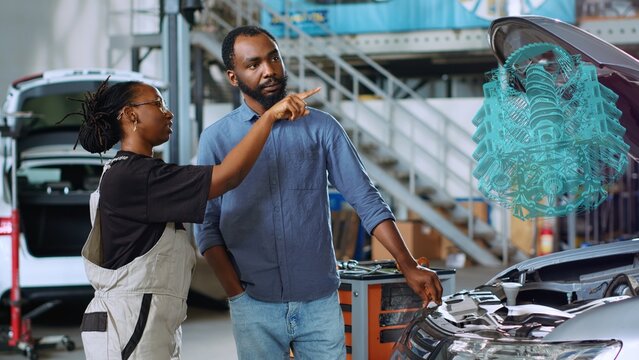 Mechanic in car service using holographic augmented reality to show woman defective components inside automobile. Experienced garage worker using advanced AR software to project vehicle engine