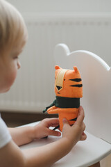 Little baby girl playing with funny small tiger toy, symbol of new 2022 in a sunny nursery