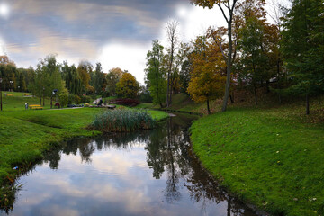 Fototapeta na wymiar Autumn landscape: a small river flows through a city park, beautiful bridges in the distance, reflection of trees in the river