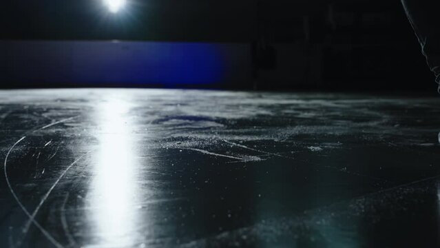 A woman ice skates on the rink, illuminated by a single backlight. The shot is a close-up from a low angle, captured in slow motion.