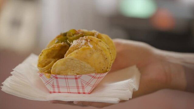 This close up video shows a hand holding vendor cheese nachos and picking a pepper off.