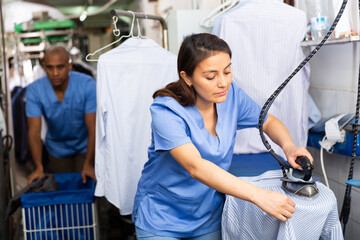 Focused woman laundry worker ironing shirt at dry-cleaning store