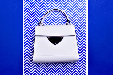 Modern female top-handle bag from white leather with black trim, metal detail, and feet isolated on...