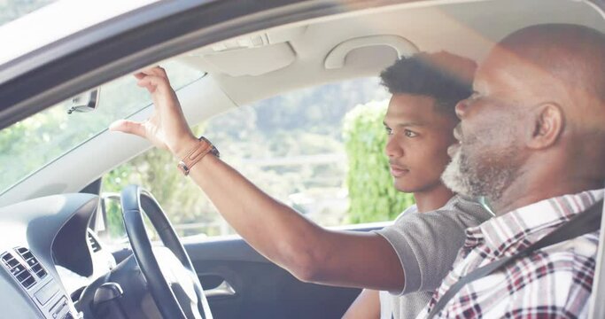 Happy african american father instructing son about mirror in car before driving lesson, slow motion