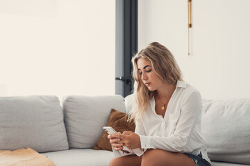 Portrait of one young attractive blonde woman using phone cell on couch relaxing surfing the net at...