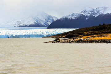 “Glaciar y Montañas en la Patagonia”. La imagen muestra un glaciar de color azul brillante que...