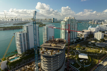 New construction site of developing residence in American urban area. Industrial tower lifting cranes in Miami, Florida. Concept of housing growth in the USA
