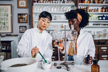 Fototapeta na wymiar Two professional multicultural pharmacists are standing in a vintage apothecary and adding ingredients while making a cure.
