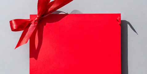 blank red gift card with red ribbon bow isolated on grey background with shadow minimal conc