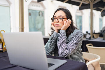 Bored inefficient woman office employee using laptop sitting at restaurant table leaning head on hands, lonely disappointed female tired of wimp work.