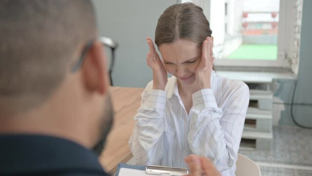 Upset female with Headache while sitting in session with Mature Counselor
