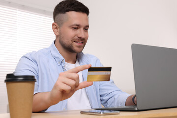 Handsome man with credit card using laptop for online shopping at table indoors