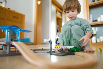 Cute toddler boy playing with wooden train set. Small child having fun with toys. Kid spending time in a cozy living room at home.