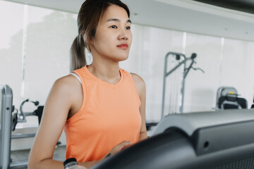 Fototapeta premium Asian woman in orange sport wears walking for exercise on treadmill in the gym.