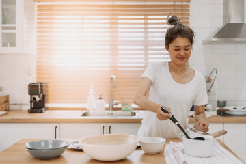 Happy asian woman serving soup into the small bowl.