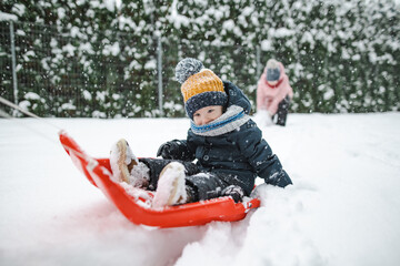 Fototapeta na wymiar Funny toddler boy having fun with a sleigh in beautiful winter park. Cute child playing in a snow.