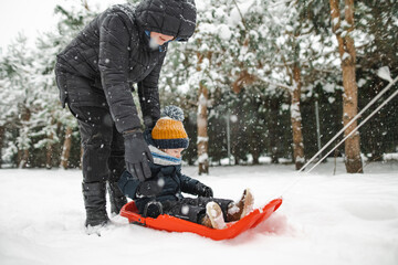 Funny toddler boy having fun with a sleigh in beautiful winter park. Cute child playing in a snow.