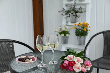 Bouquet of roses, glasses with wine and candies on glass table on outdoor terrace
