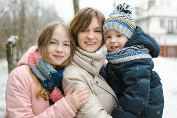 Two big sisters and their toddler brother having fun outdoors. Two young girls holding their sibling boy on winter day. Kids during winter break.