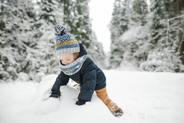 Cute toddler boy having fun on a walk in snow covered pine forest on chilly winter day. Child exploring nature.