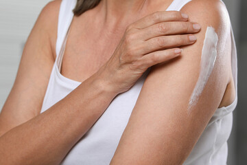 Woman applying body cream onto arm on blurred background, closeup